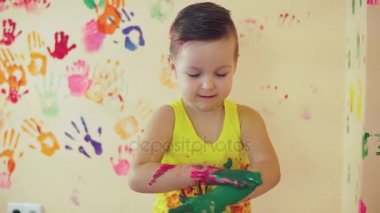Sevimli küçük çocuk boyalı ellerle veiw kadar duvara onun renkli el izleri bırakarak ve parmağını gösterilmesini sonra kapatın. Genç, mutlu bir aile. Anne ve çocuk kavramı