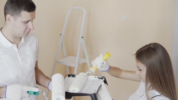 La mujer sostiene el rodillo con pintura lista para mezclar. Pareja joven decorar su nuevo apartamento. El joven esposo y la esposa están pintando la pared. Hermosa pareja haciendo reparaciones en su nuevo piso . — Vídeos de Stock