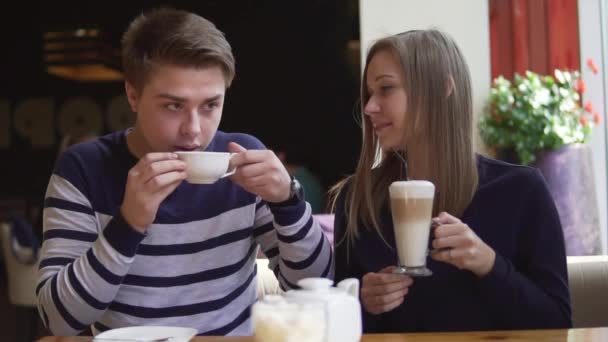 Mladá usmívající se pár ve venkovní kavárně s úsměvem a pití kávy. Slowmotion. — Stock video