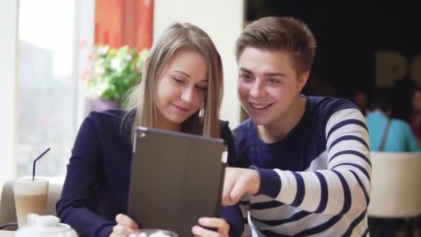 Joven pareja atractiva usando tableta digital, mirando a la pantalla en la cafetería . — Vídeo de stock