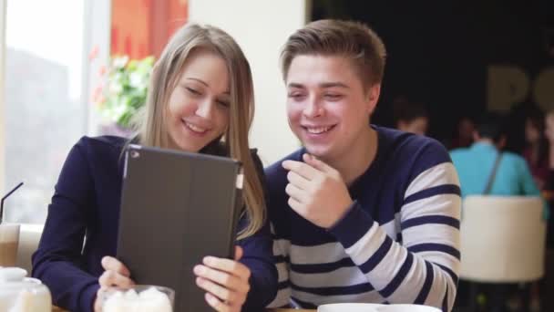 Joven pareja atractiva usando tableta digital, mirando a la pantalla en la cafetería . — Vídeo de stock