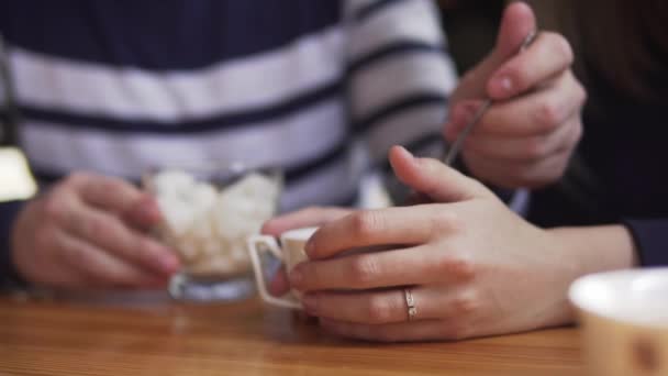 Hombre poniendo cubo de azúcar a la taza de té, usando cuchara, tiro de cerca. Cafetería ordinaria, las manos de las mujeres están sosteniendo la taza de té. El cubo de azúcar se recoge y se deja caer en la bebida caliente. Lento. . — Vídeo de stock