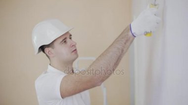Kask bir rulo ile bir duvar boyama iş yerinde genç ressamın adam.