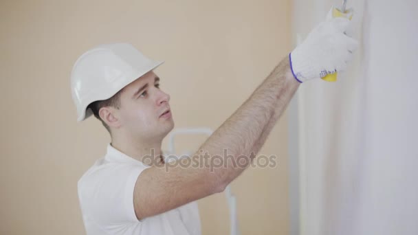 junger Maler mit Helm bei der Arbeit beim Bemalen einer Wand mit einer Farbrolle.