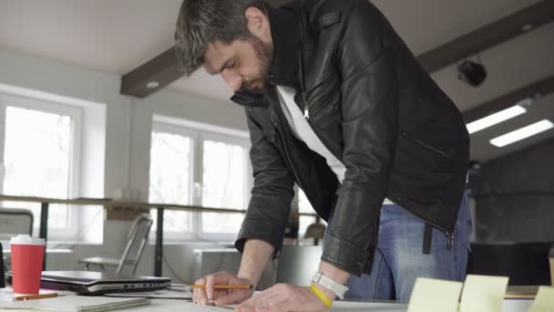 Joven trabajando en un proyecto, dibujando y pensando en la oficina moderna. Taza de café y portátil en la mesa. Disparo en 4k . — Vídeos de Stock