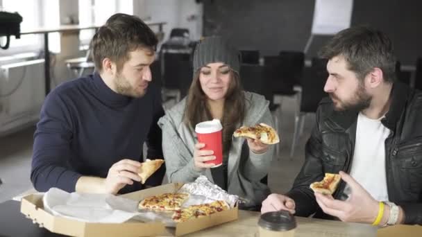 Un grupo de jóvenes diseñadores liderados por el jefe están trabajando en el proyecto de oficina de diseño y comer pizza entregada y beber té o café en tazas de papel. Disparo en 4k — Vídeos de Stock