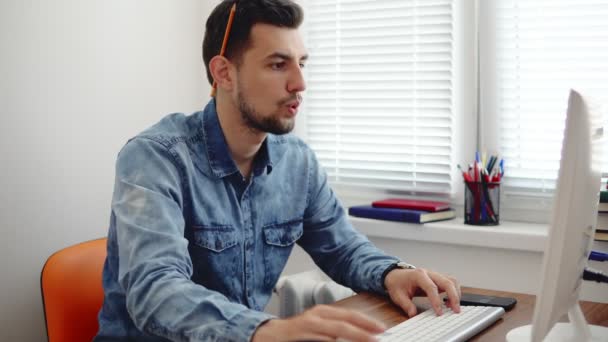 Tânărul om de afaceri lucrează la calculator într-un birou modern elegant și ia notițe folosind creionul și caietul. Computer, telefon şi ceaşcă pe masă. Împușcat în 4k — Videoclip de stoc