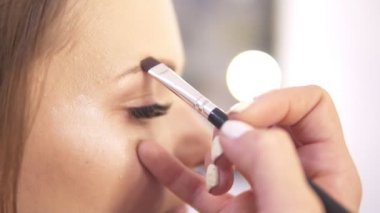 Portre fotoğraf çekimi için onu hazırlarken bir manken kaşları fırçalama bir makyaj sanatçısı görünümünü. Slowmotion atış