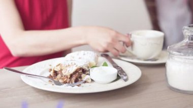 Kahve içme ve tatlı meyveli turta çatal ve bıçak kullanarak restoranda yemek Kırmızı elbiseli kız tanınmaz. Güzel beyaz fincan kahve masada. Slowmotion atış.