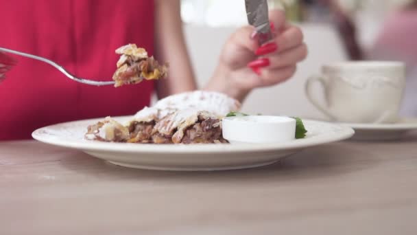 Oigenkännlig flicka i röd klänning äta efterrätt strudel på restaurangen med gaffel och kniv. Vackra vita koppen med kaffe på bordet. Slowmotion skott. — Stockvideo