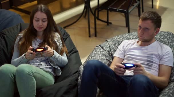 Молодая пара играет в видеоигры дома. Стрельба и управление с помощью игрового контроллера. Xbox и Playstation. Беспроводной игровой контроллер. Слоумоушн — стоковое видео