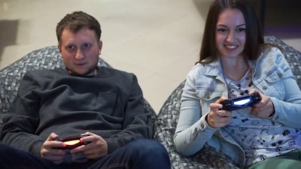 Молодая пара играет в видеоигры дома. Стрельба и управление с помощью игрового контроллера. Xbox и Playstation. Беспроводной игровой контроллер. Слоумоушн — стоковое видео
