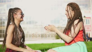 Mutlu kadın yaz Park çimenlerin üzerinde oturan dreads ile. Söz ve açık havada eğleniyor oynayan genç arkadaşlar. Melez kadın sarışın kadınla konuşuyor. Slowmotion atış
