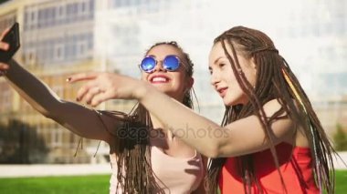 Mutlu kadın yaz Park çimenlerin üzerinde oturan ve selfies konuşurken dreads ile. Açık havada poz ve having fun konuşuyor ve çekim, genç arkadaşlarım. Slowmotion atış