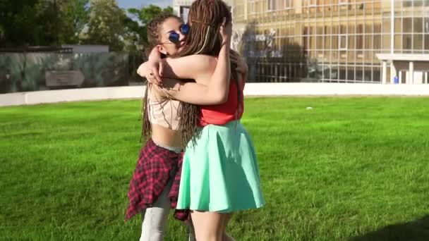 Twee gelukkige jonge meisjes met dreadlocks knuffelen elkaar. Opgewonden vrouwelijke vrienden omhelzen elkaar en lachen tijdens de zonnige dag in het park. Womens vriendschap. Tikje schot — Stockvideo
