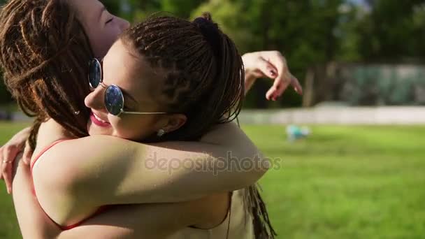 Дві щасливі молоді дівчата з мріями обіймають один одного. Захоплені друзі-жінки обіймаються і сміються під час сонячного дня в парку. Жіноча дружба. Постріл уповільнення — стокове відео