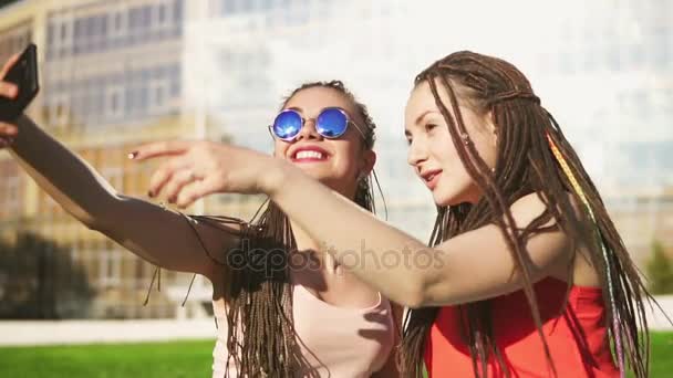 Mujeres felices con temores sentados en la hierba en el parque de verano y hablando selfies. Jóvenes amigos hablando y tomando fotos, posando al aire libre y divirtiéndose. Disparo en cámara lenta — Vídeos de Stock