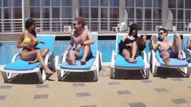 Havuz kenarında şezlong üzerinde yalan ve eğlenerek mutlu genç insanlar. Resort Yüzme Havuzu rahatlatıcı. Otel, tatil sırasında konuşan kadın ve erkekler. Slowmotion atış
