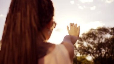 Closeup arkadan görünüm bir kadının güneşe bakarak ve kendini güneşin eliyle kimden saklanıyor. Genç kadın bir güneş ile oynarken dreads ile. Slowmotion atış.