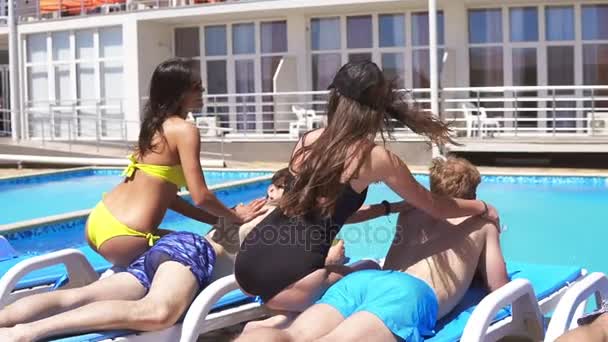 Three men receiving massage from attractive young girls in bikini lying on coaches by the pool at a beautiful villa and drinking beer. Slowmotion shot. — Stock Video