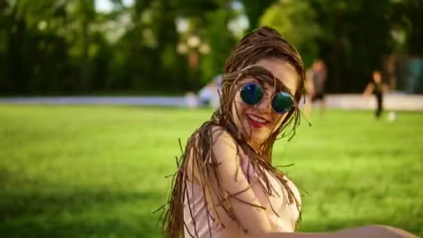 Młoda, piękna dziewczyna z dredy taniec w parku. Piękna kobieta w dżinsy i okulary przeciwsłoneczne, słuchanie muzyki i tańca w słoneczne dni. Slowmotion strzał. — Wideo stockowe
