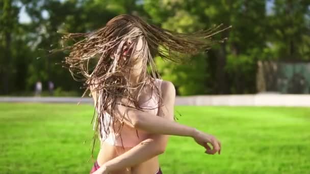 Молодая красивая девушка с дредами танцует в парке. Красивая женщина слушает музыку и танцует в солнечный день. Слоумоушн . — стоковое видео