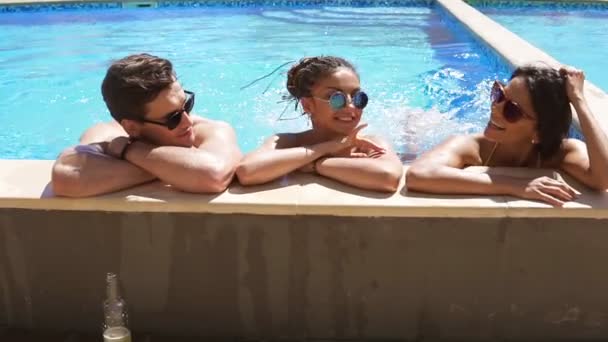 Grupo feliz de amigos desfrutando de festa na piscina de verão salpicando e chutando suas pernas na água. Jovens pessoas atraentes saindo e conversando ao lado da piscina no verão . — Vídeo de Stock