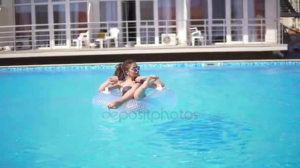 Menina sexy com óculos de sol, coquetel e dreads no anel de borracha inflável posando na piscina. Tiro em câmara lenta . — Vídeo de Stock