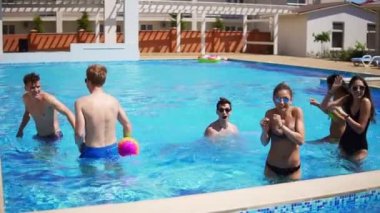 Grup genç arkadaşlar yüzme havuzunda voleybolu top oynarken. Yaz aylarında havuz partisi. Slowmotion atış