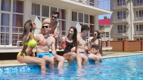 Happy group of young friends hanging out with coctails and chatting at the side of the pool in the summertime. Pool party. Slowmotion shot — Stock Video