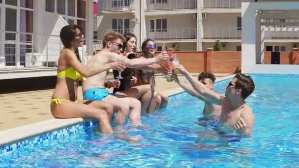 Feliz grupo de jóvenes amigos pasando el rato con cócteles y charlando al lado de la piscina en el verano. ¡Salud! Fiesta en la piscina. Disparo en cámara lenta — Vídeo de stock