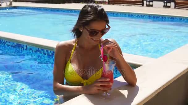 Mooie jonge vrouwelijke toeristische drinken een cocktail ontspannen aan de rand van een resort zwembad in het water af te koelen op een warme zomerdag. Tikje schot — Stockvideo