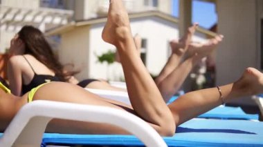 Kadın arkadaşları rahatlatıcı ile kokteyller havuz başında içme güneş gözlüğü güzel genç kız. Bacaklar closeup görünümü. Yaz aylarında havuz partisi. Slowmotion atış
