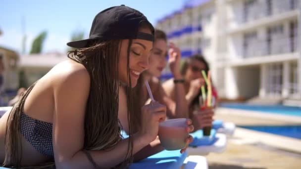 Bella ragazza con i dreads bere cocktail con le sue amiche di relax a bordo piscina. Festa estiva in piscina. Colpo di rallentamento — Video Stock