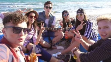 Bir video kaydı ya da selfie grup easychairs üzerinde sahilde oturup, gitar çalmak ve bir yaz akşamı şarkı arkadaşıyla alarak genç adam. Slowmotion atış
