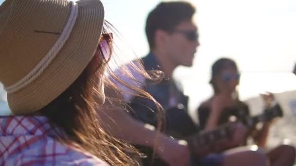 Giovane che suona la chitarra tra un gruppo di amici seduti su sedie a rotelle sulla spiaggia e canta in una serata estiva. Colpo di rallentamento — Video Stock