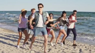 Grup genç hipster arkadaşıyla birlikte çalışan bir sahilde sular kenarında. Slowmotion atış