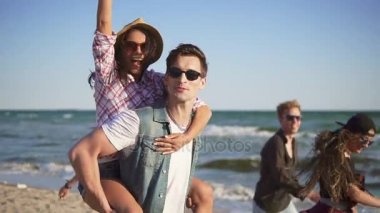 Eğleniyor çift sırtlama gülüyor mutlu, neşeli ve eğlenceli, insanların doğa manzara plaj tarafından zevk genç grup ile birlikte yapıyor. Slowmotion atış