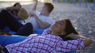 Sandalye üzerinde döşeme ve sahilde arkadaş grubu arasında bir gün batımı sırasında gülümseyen mutlu genç kadın. Slowmotion atış