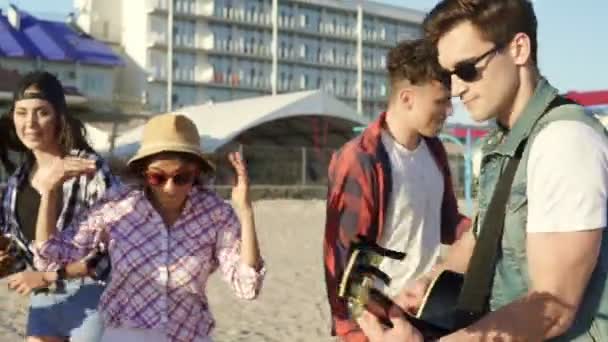 Літня вечірка на пляжі. Молоді хлопчики та дівчатка п'ють коктейлі, танцюючи разом, граючи на гітарі та співаючи пісні на пляжі на краю води. Постріл уповільнення — стокове відео