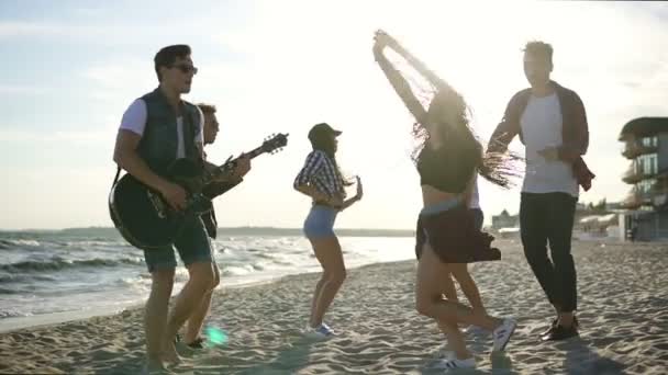 Sommar party på stranden. Unga vänner dricka cocktails, Dans i cirkle, spelar gitarr, edge sjunger sånger och klappa på en strand på waters under solnedgången. Slowmotion skott — Stockvideo