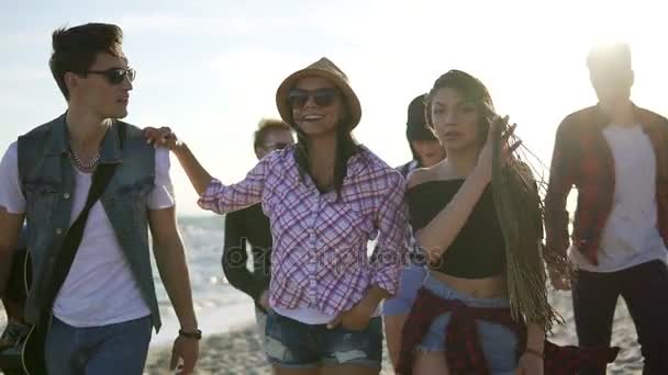 Grupo de jóvenes amigos hipster caminando juntos en una playa en el borde del agua sosteniendo una guitarra. Disparo en cámara lenta — Vídeos de Stock