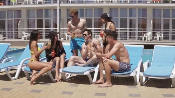 Grupo de belos jovens amigos bebendo coquetéis e se divertindo sentados na piscina. Tiros em 4K — Vídeo de Stock