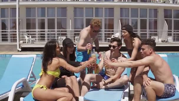 Groep van mooie jonge vrienden in zwemkleding drinken van cocktails met gejuich en plezier zitten bij het zwembad. Schot in 4k — Stockvideo