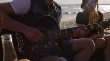 Bira içme, sahilde easychairs üzerinde oturan ve bir yaz akşamı gitar çalmak bir arkadaşına dinleme genç mutlu arkadaşlar. 4 k'dan fazla vurdu