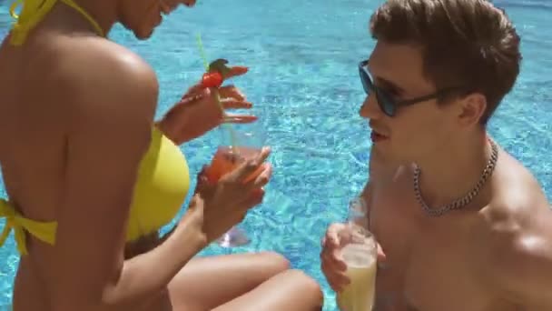 Молодая взрослая пара флиртует и разговаривает в бассейне, пьет коктейли, делает ура. Летняя вечеринка у бассейна. Выстрел в 4k — стоковое видео