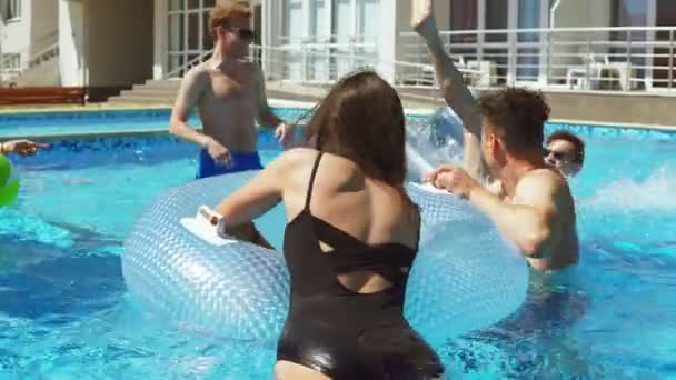 Молодые привлекательные люди плавают на надувных трубах на вечеринке у бассейна. Красивые женщины и мужчины устраивают вечеринку у бассейна. Выстрел в 4k — стоковое видео
