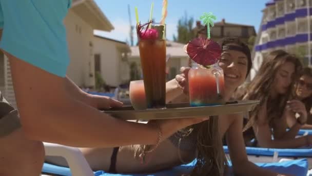 Um garçom masculino irreconhecível trazendo coquetéis para meninas bonitas relaxando na piscina. Festa da piscina no Verão. Tiros em 4K — Vídeo de Stock