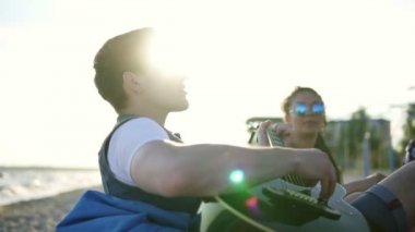 Genç adam sahilde easychairs üzerinde oturan ve bir yaz akşamı bir gün batımı sırasında şarkı arkadaş grubu arasında gitar çalıyor. Slowmotion atış