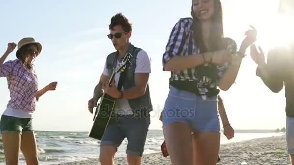 Fiesta de verano en la playa. Niños y niñas aplaudiendo, bailando juntos tocando la guitarra y cantando canciones en una playa en el borde del mar. Disparo en cámara lenta — Vídeo de stock